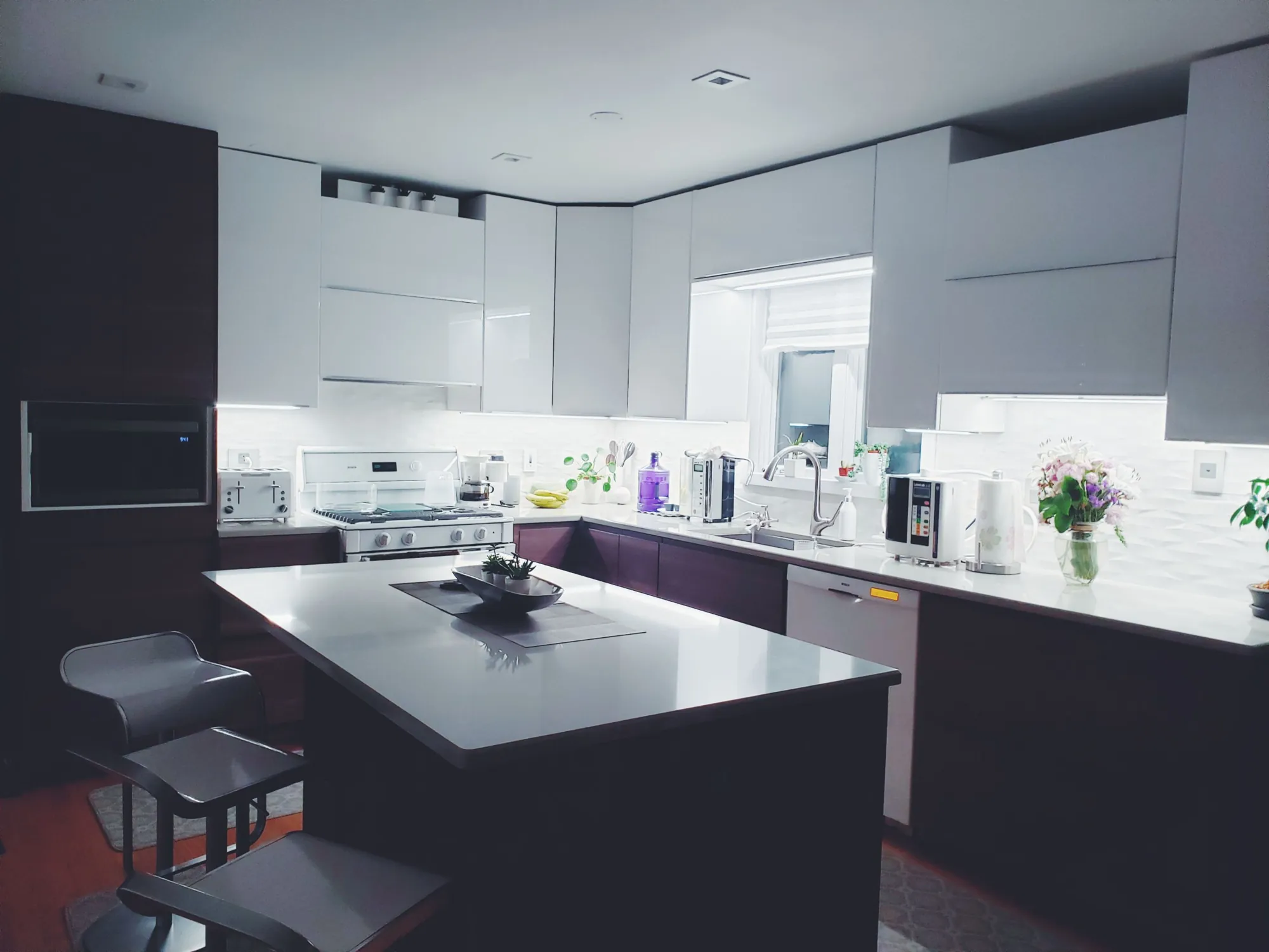 Kitchen with white gloss upper cabinets, dark lower cabinets and a quartz island